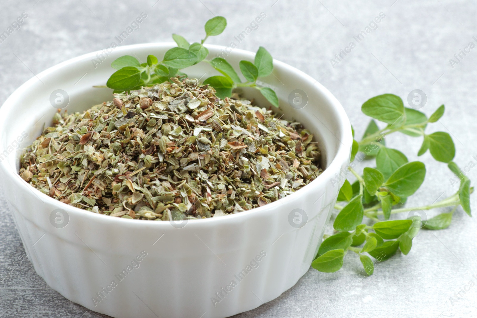 Photo of Dried oregano in bowl and green leaves on light grey table, closeup