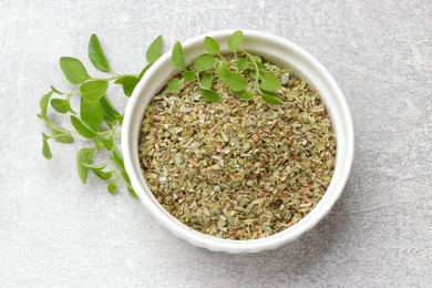 Dried oregano in bowl and green leaves on light grey table, top view