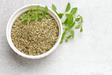 Dried oregano in bowl and green leaves on light grey table, top view. Space for text