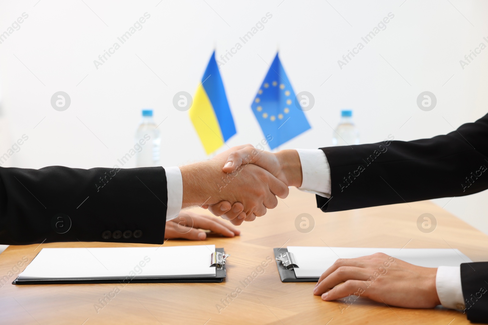 Photo of Diplomats shaking hands during meeting at wooden table indoors, closeup