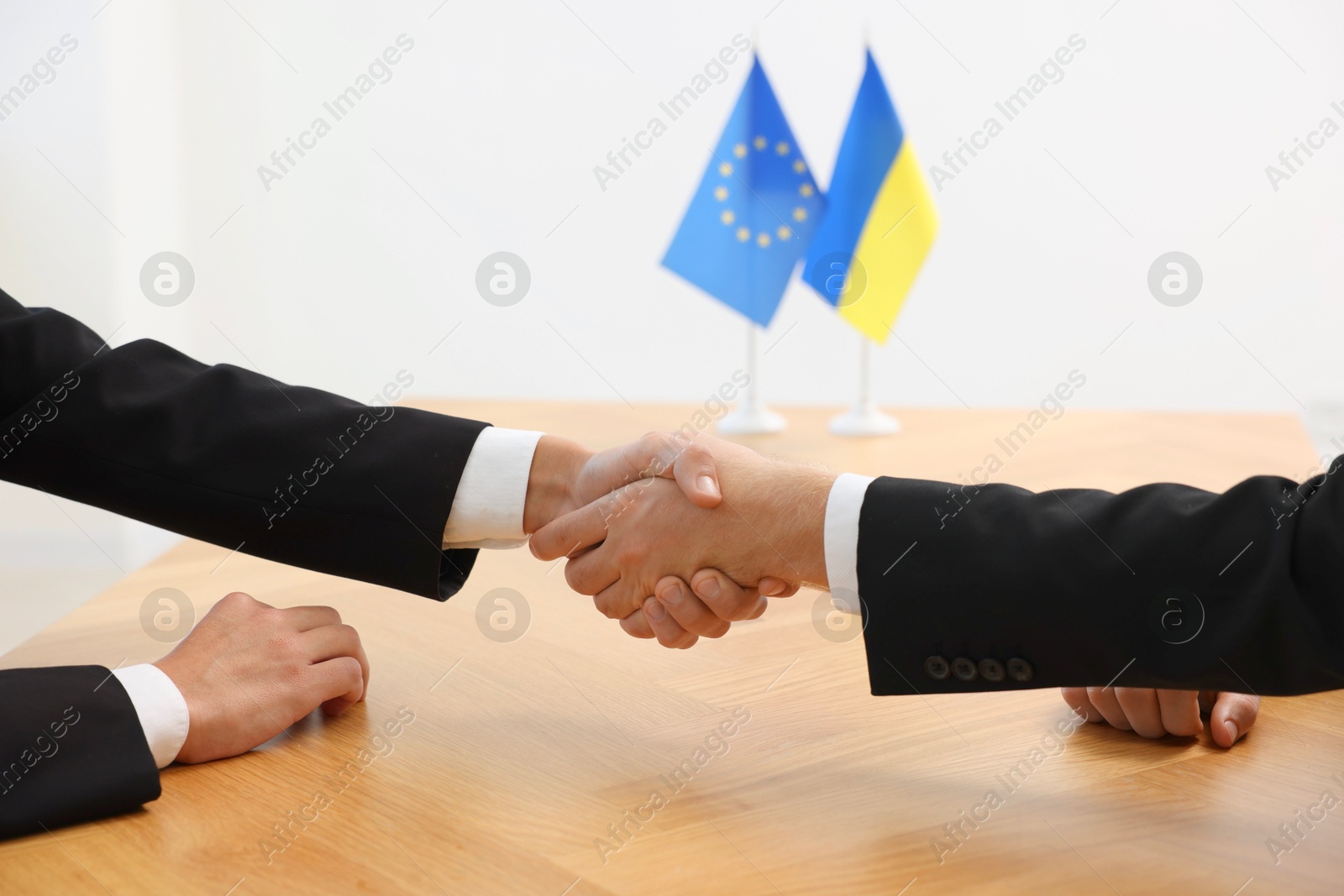 Photo of Diplomats shaking hands during meeting at wooden table indoors, closeup