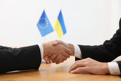 Photo of Diplomats shaking hands during meeting at wooden table indoors, closeup