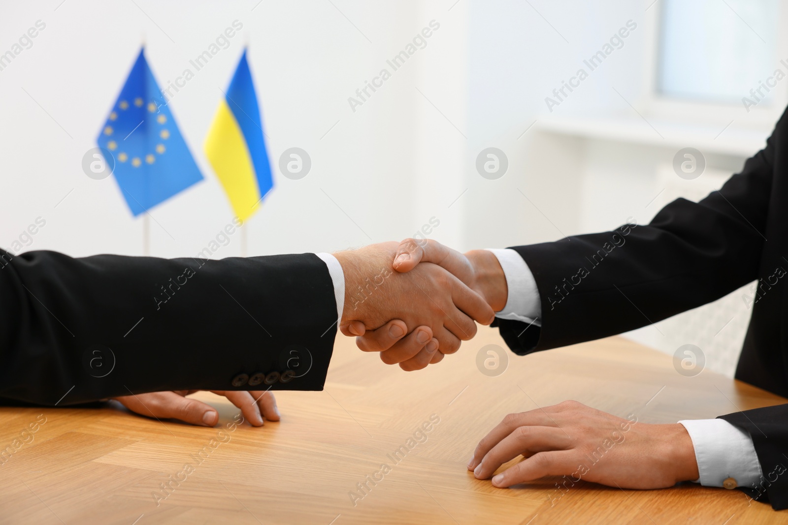 Photo of Diplomats shaking hands during meeting at wooden table indoors, closeup