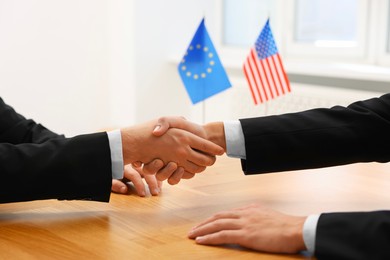 Photo of Diplomats shaking hands during meeting at wooden table indoors, closeup