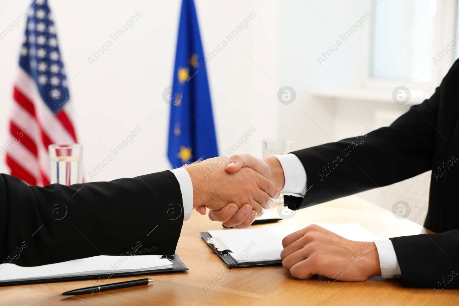 Photo of Diplomats shaking hands during meeting at wooden table indoors, closeup