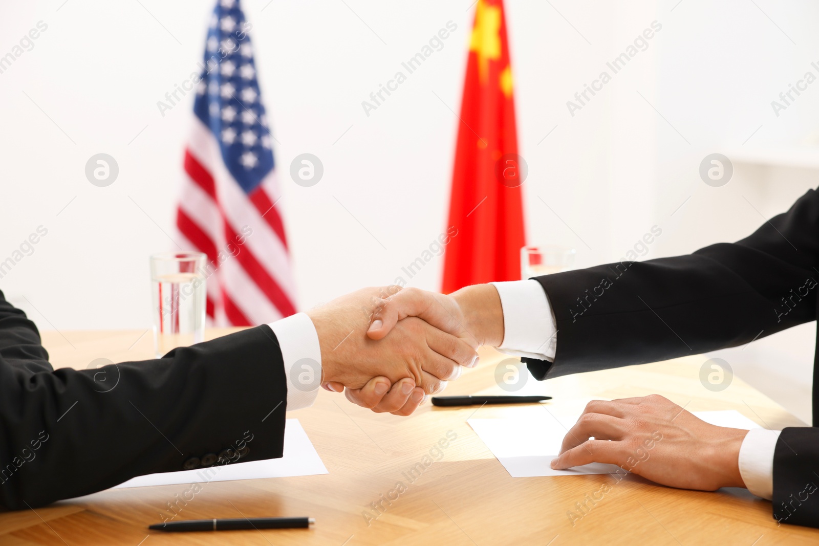 Photo of Diplomats shaking hands during meeting at wooden table indoors, closeup