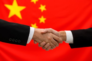 Photo of Diplomats shaking hands against flag of China, closeup