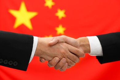 Photo of Diplomats shaking hands against flag of China, closeup