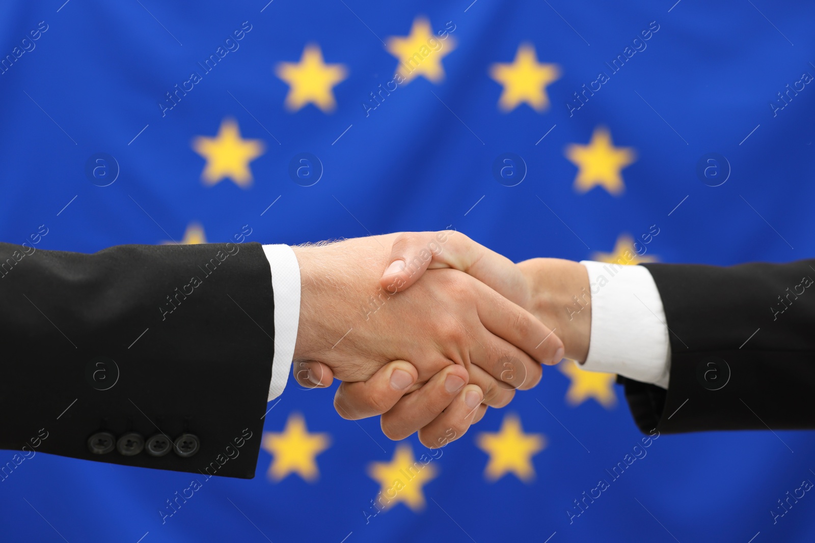 Photo of Diplomats shaking hands against flag of European Union, closeup