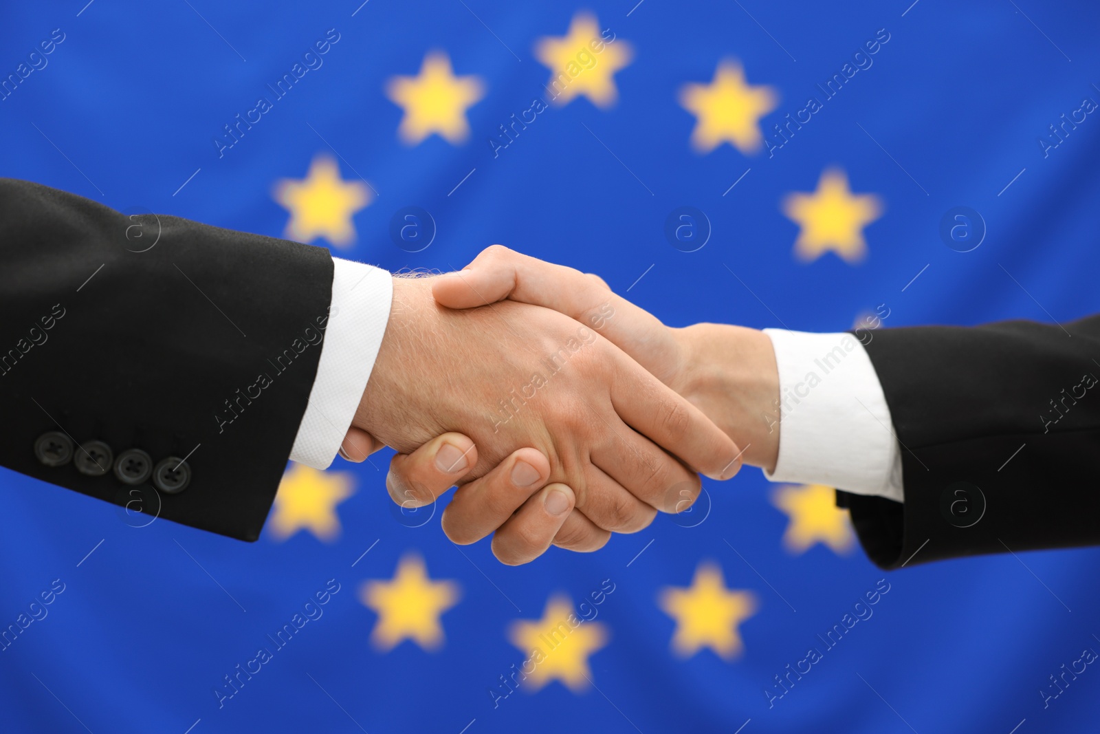 Photo of Diplomats shaking hands against flag of European Union, closeup