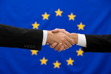 Photo of Diplomats shaking hands against flag of European Union, closeup