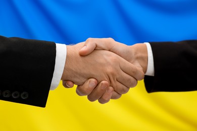 Photo of Diplomats shaking hands against flag of Ukraine, closeup