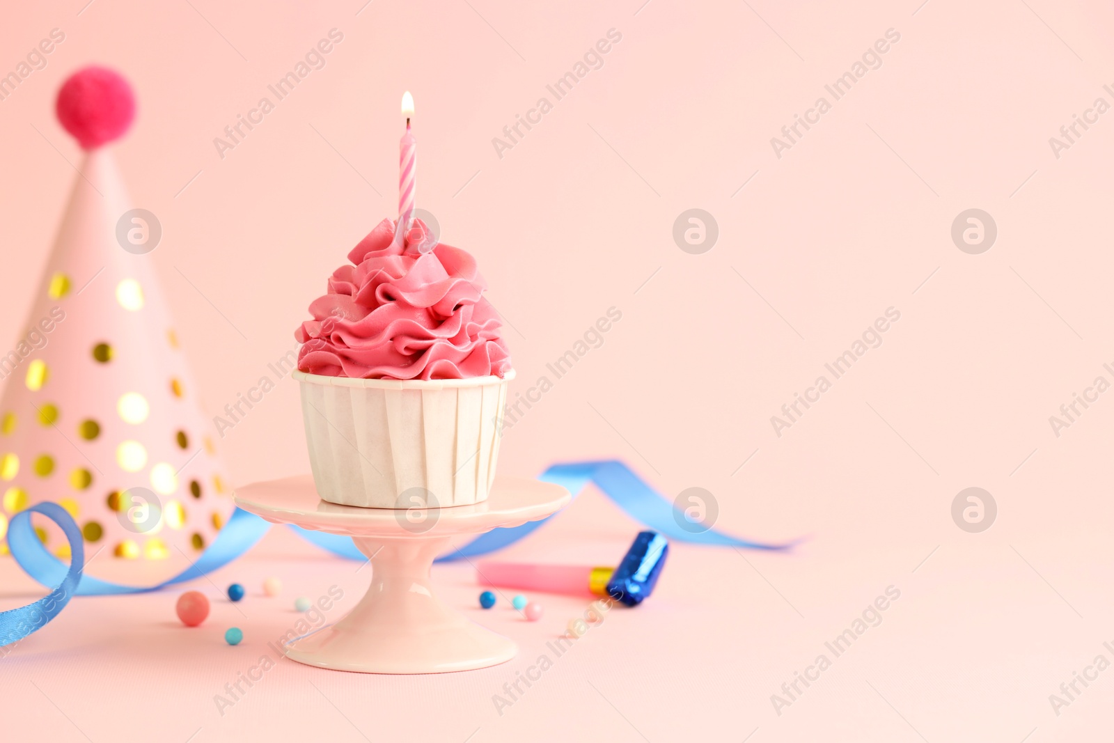 Photo of Tasty cupcake with burning candle and party cone on pink background, space for text