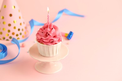 Photo of Tasty cupcake with burning candle and party cone on pink background, space for text