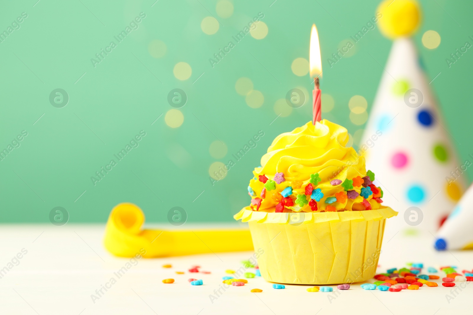 Photo of Tasty cupcake with burning candle and party cones on green background with blurred lights, space for text