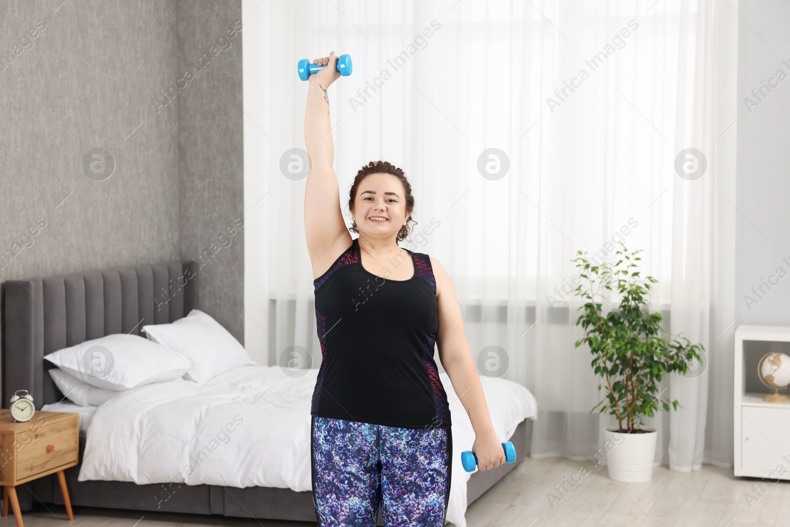 Photo of Plus size woman with dumbbells training at home