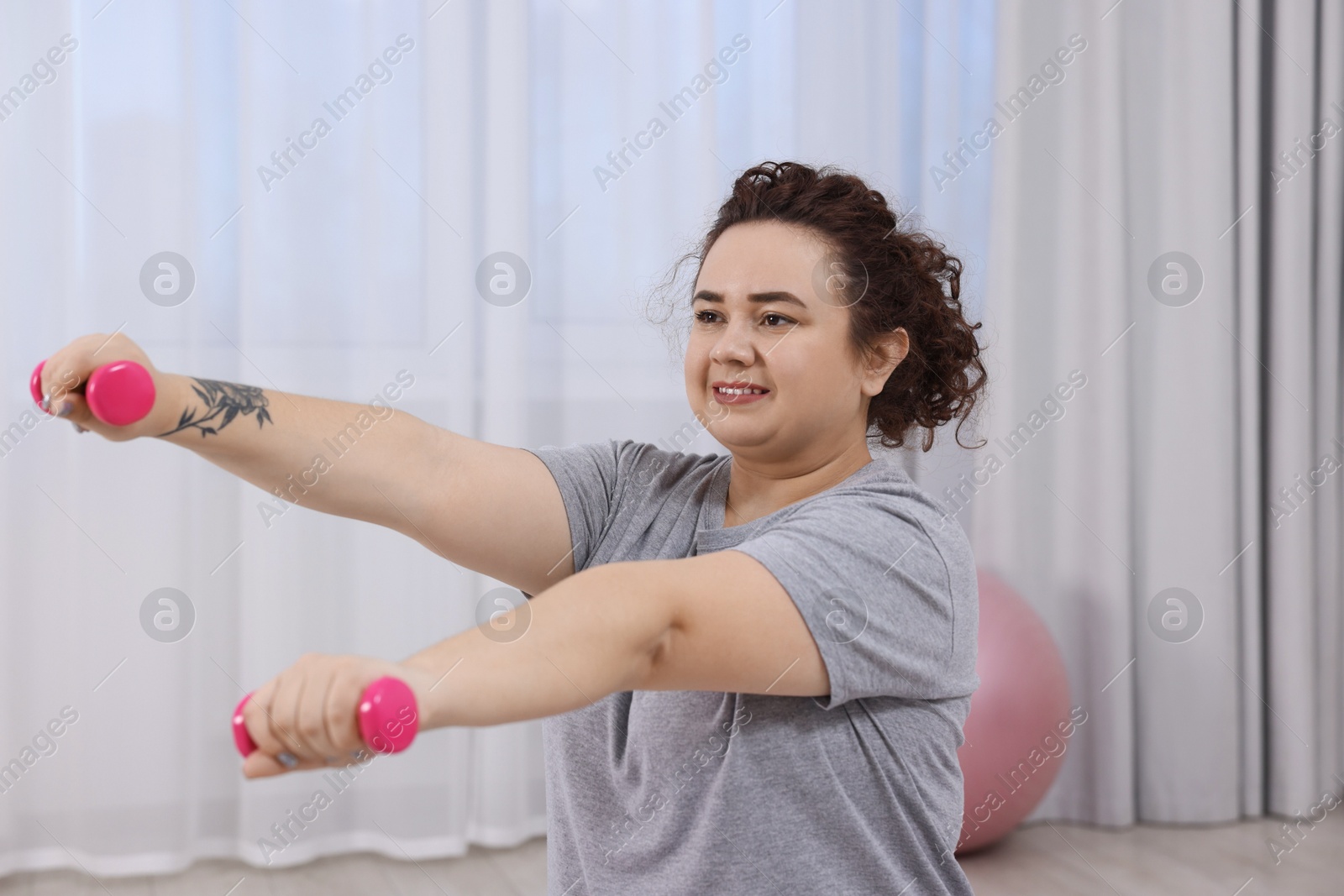 Photo of Plus size woman with dumbbells training at home