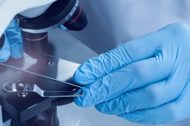 Photo of Scientist examining sample on slide under microscope, closeup