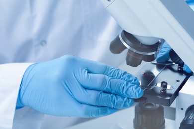 Photo of Scientist examining sample on slide under microscope, closeup