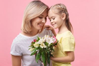 Little daughter congratulating her mom with bouquet of alstroemeria flowers on pink background. Happy Mother's Day