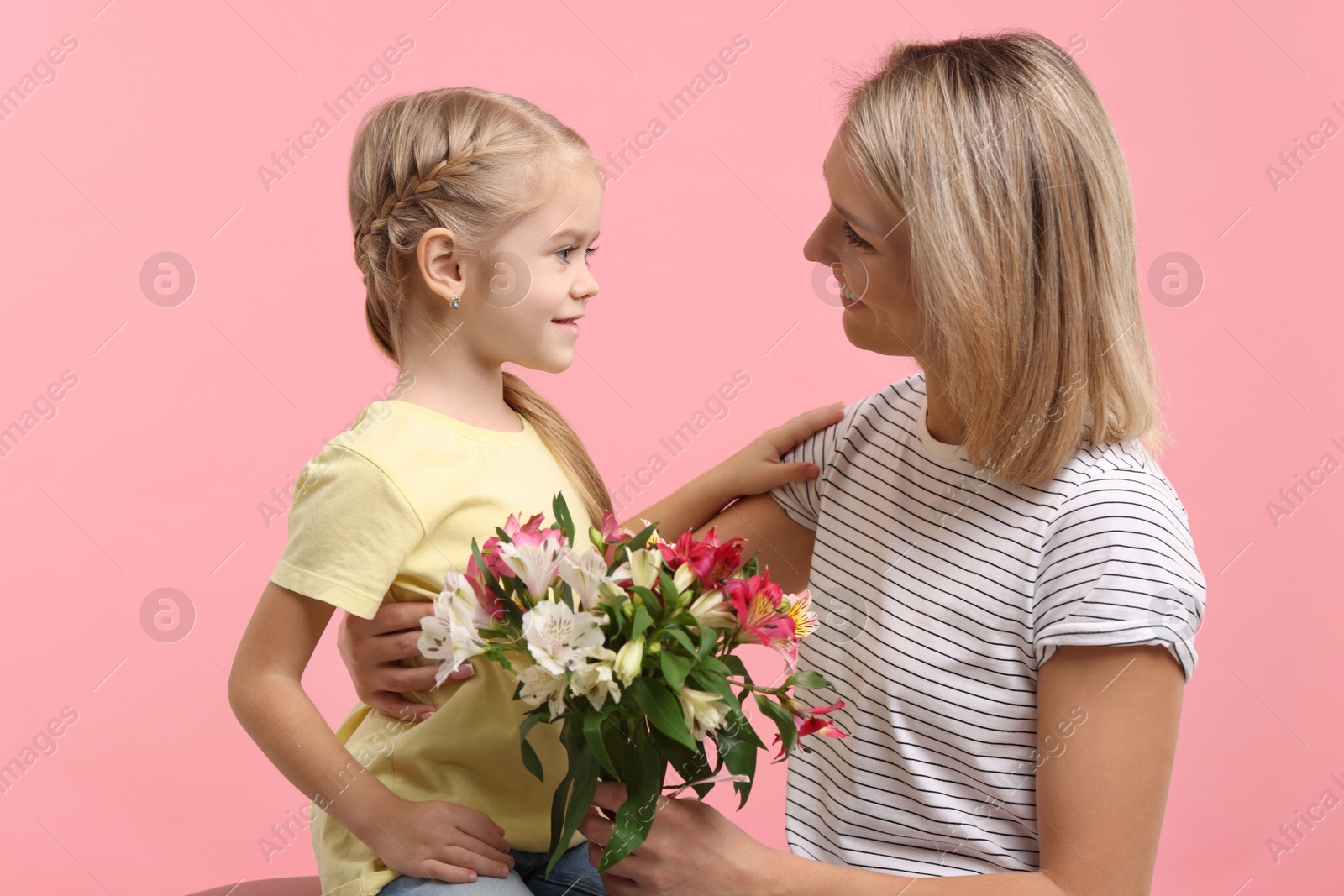 Photo of Little daughter congratulating her mom with bouquet of alstroemeria flowers on pink background. Happy Mother's Day