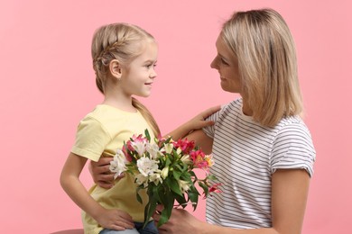 Photo of Little daughter congratulating her mom with bouquet of alstroemeria flowers on pink background. Happy Mother's Day