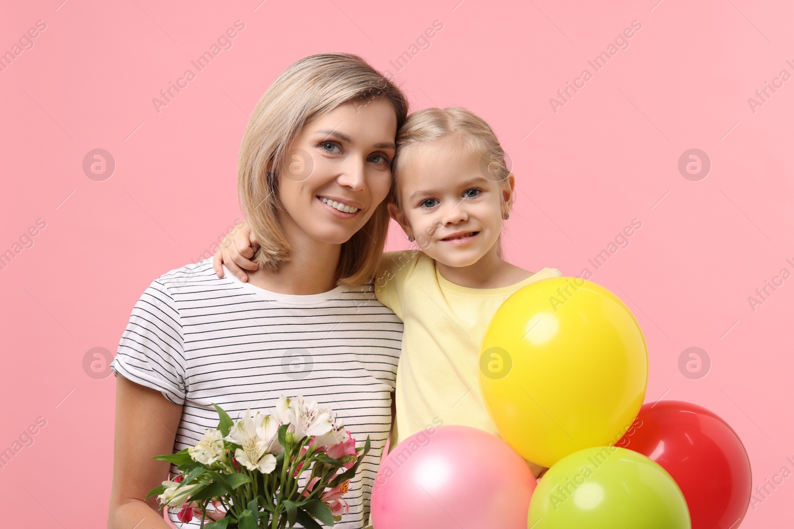 Photo of Little daughter congratulating her mom with bouquet of alstroemeria flowers and balloons on pink background. Happy Mother's Day