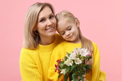 Photo of Happy woman with her daughter and bouquet of alstroemeria flowers on pink background. Mother's Day celebration