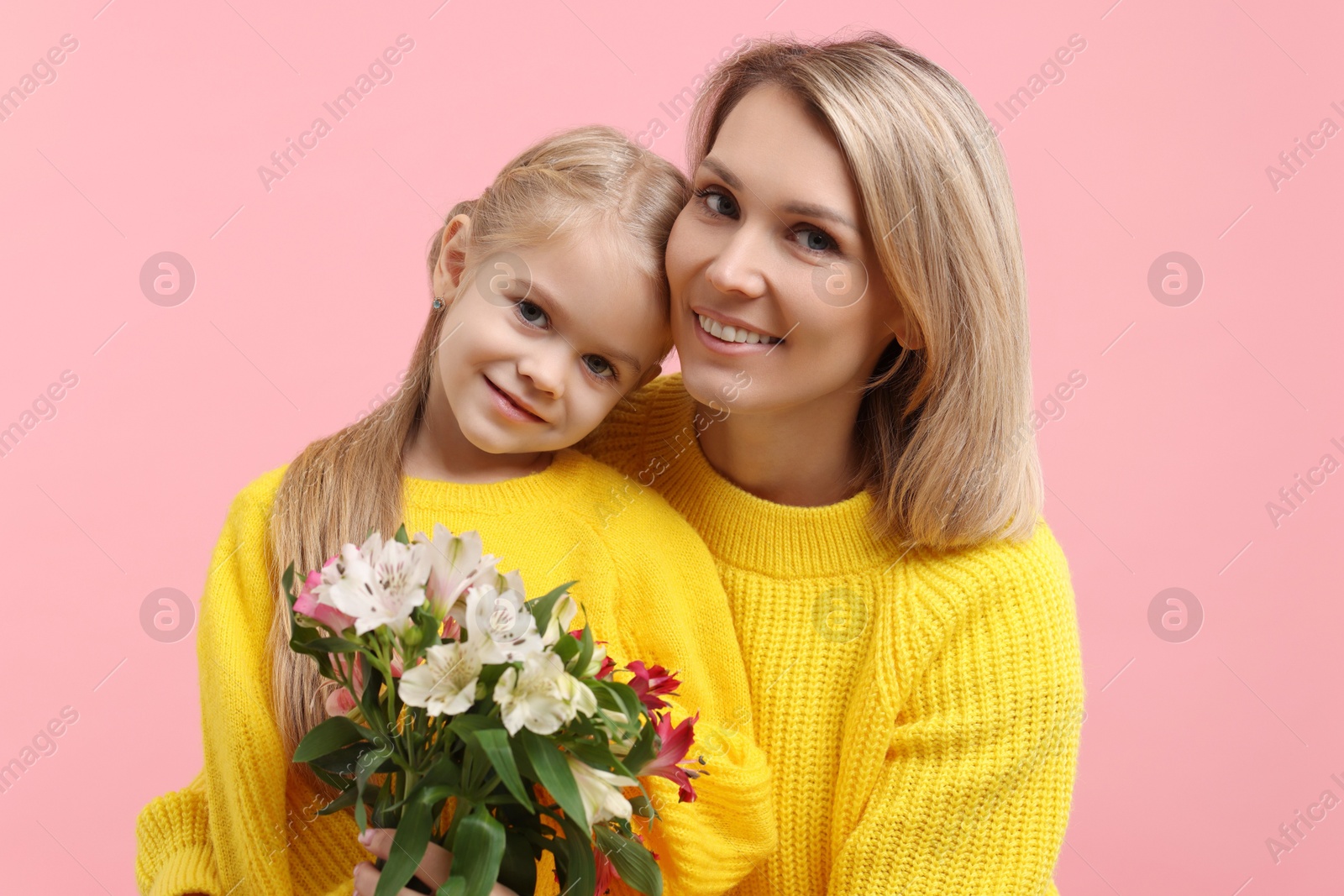 Photo of Happy woman with her daughter and bouquet of alstroemeria flowers on pink background. Mother's Day celebration