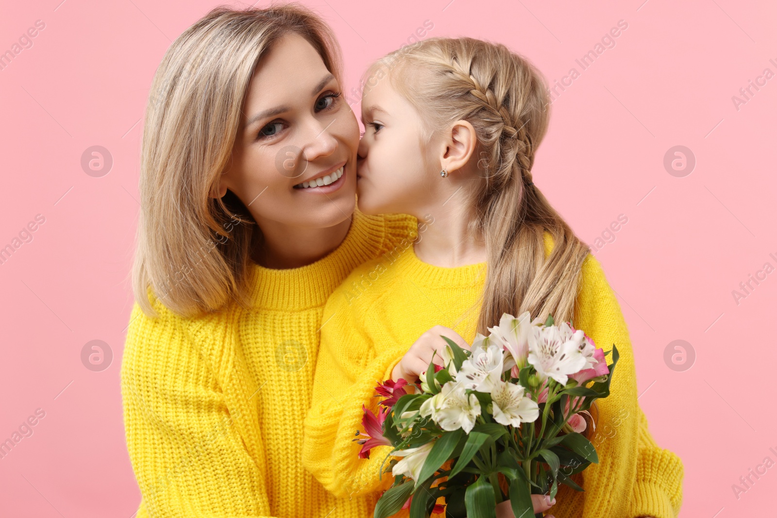 Photo of Happy woman with her daughter and bouquet of alstroemeria flowers on pink background. Mother's Day celebration