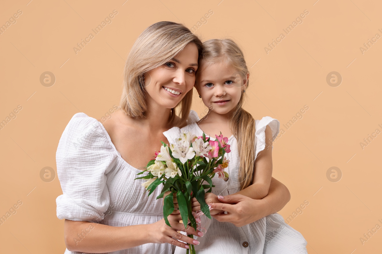 Photo of Happy woman with her daughter and bouquet of alstroemeria flowers on beige background. Mother's Day celebration