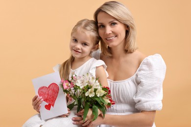 Photo of Happy woman with her daughter, bouquet of alstroemeria flowers and greeting card on beige background. Mother's Day celebration