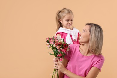 Photo of Little daughter congratulating her mom with bouquet of alstroemeria flowers on beige background, space for text. Happy Mother's Day