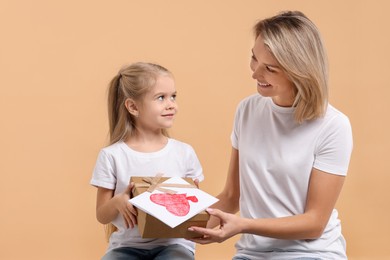 Photo of Happy woman with her daughter and greeting card on beige background. Mother's Day celebration