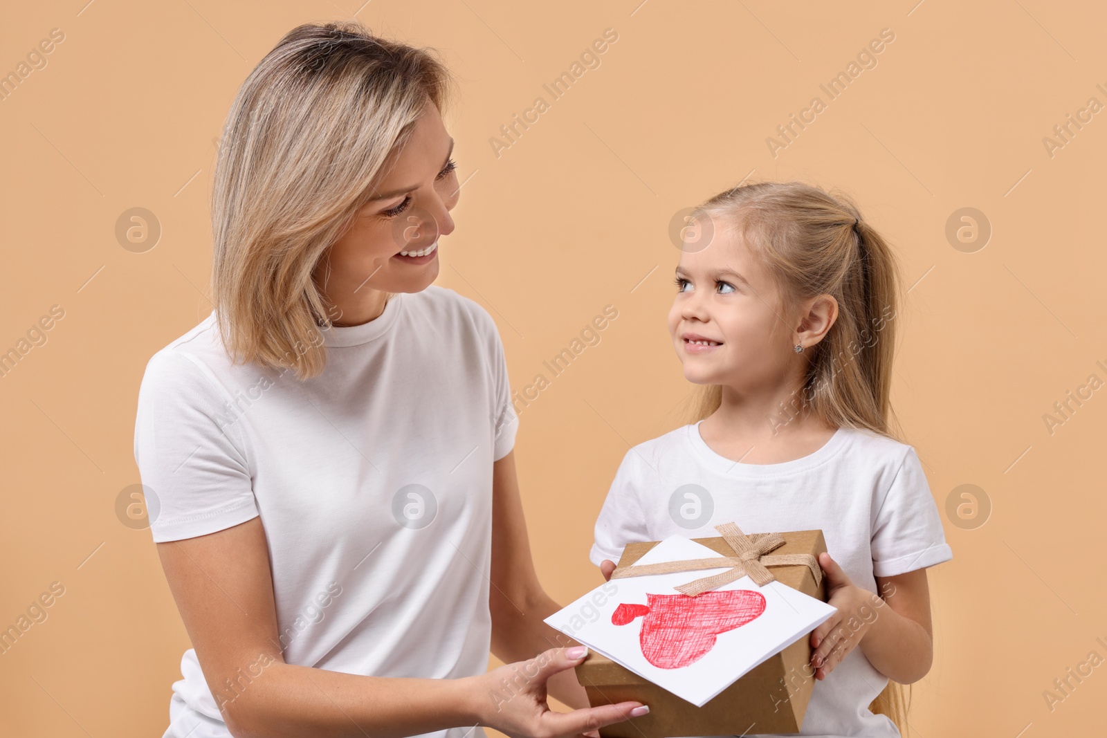 Photo of Happy woman with her daughter and greeting card on beige background. Mother's Day celebration