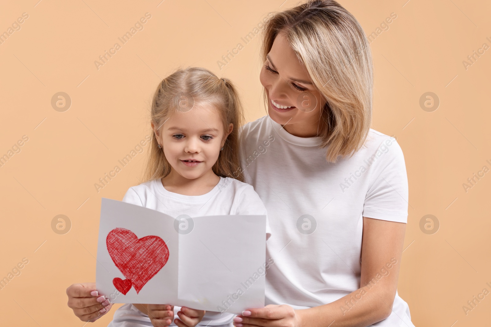 Photo of Happy woman with her daughter and greeting card on beige background. Mother's Day celebration