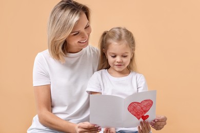 Photo of Happy woman with her daughter and greeting card on beige background. Mother's Day celebration