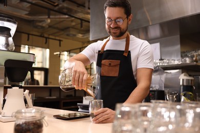 Photo of Barista pouring coffee from glass coffeemaker into cup at table in cafe