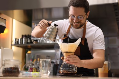 Barista brewing coffee in glass coffeemaker with paper filter at table in cafe