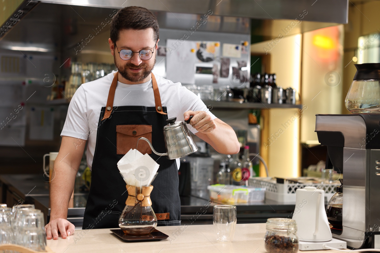 Photo of Barista brewing coffee in glass coffeemaker with paper filter at table in cafe