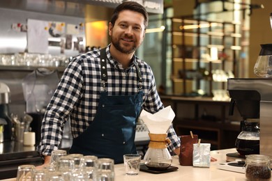 Barista with glass coffeemaker at table in cafe