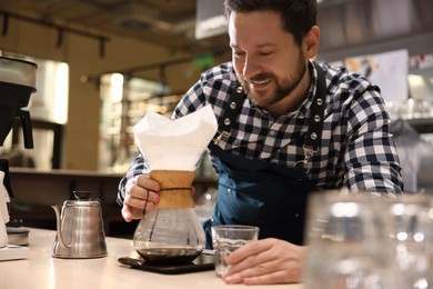 Photo of Barista making coffee with glass coffeemaker at table in cafe