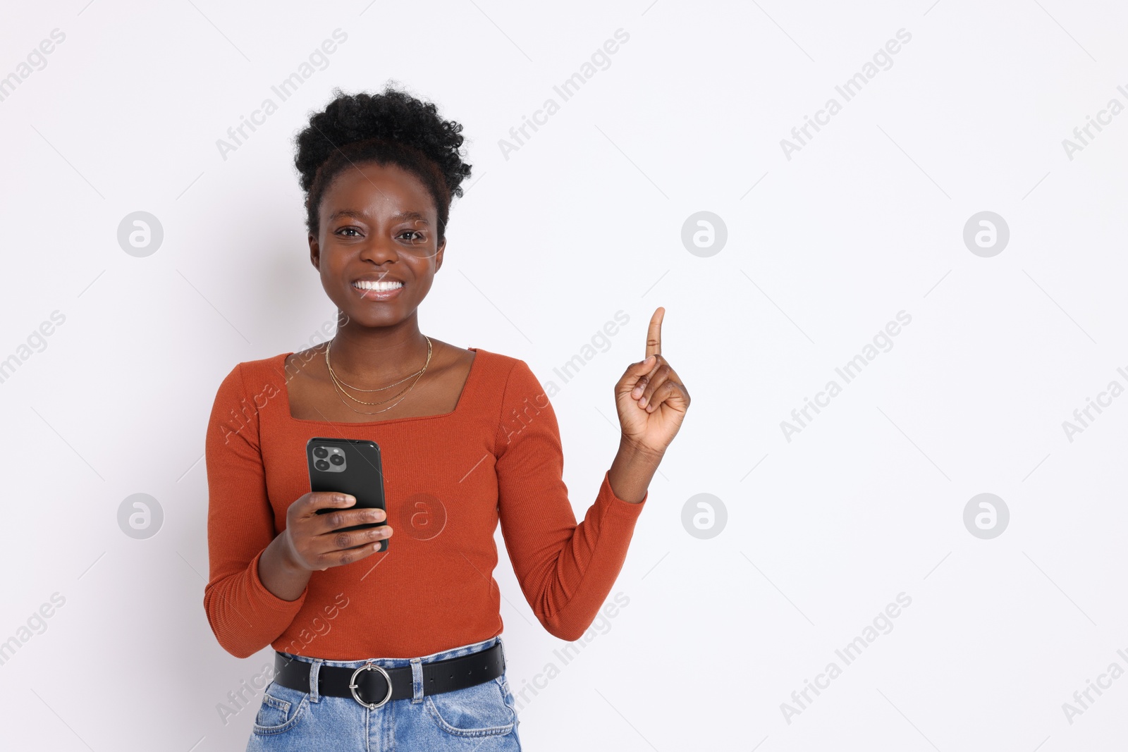 Photo of Cheerful woman with smartphone pointing at something on white background. Space for text