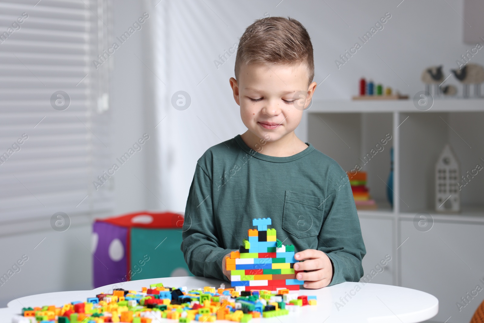 Photo of Cute boy playing with building blocks at white table indoors