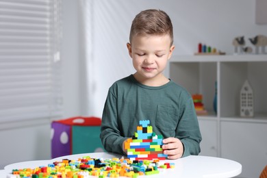 Photo of Cute boy playing with building blocks at white table indoors