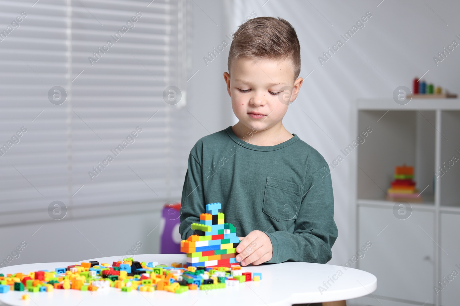 Photo of Cute boy playing with building blocks at white table indoors