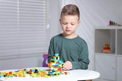 Photo of Cute boy playing with building blocks at white table indoors