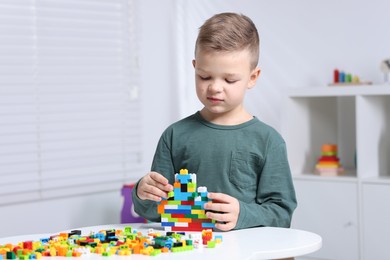 Photo of Cute boy playing with building blocks at white table indoors. Space for text