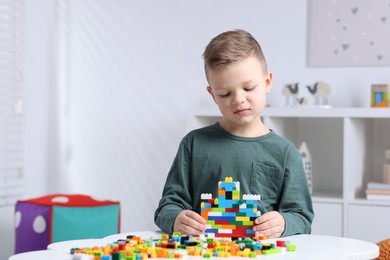 Photo of Cute boy playing with building blocks at white table indoors. Space for text