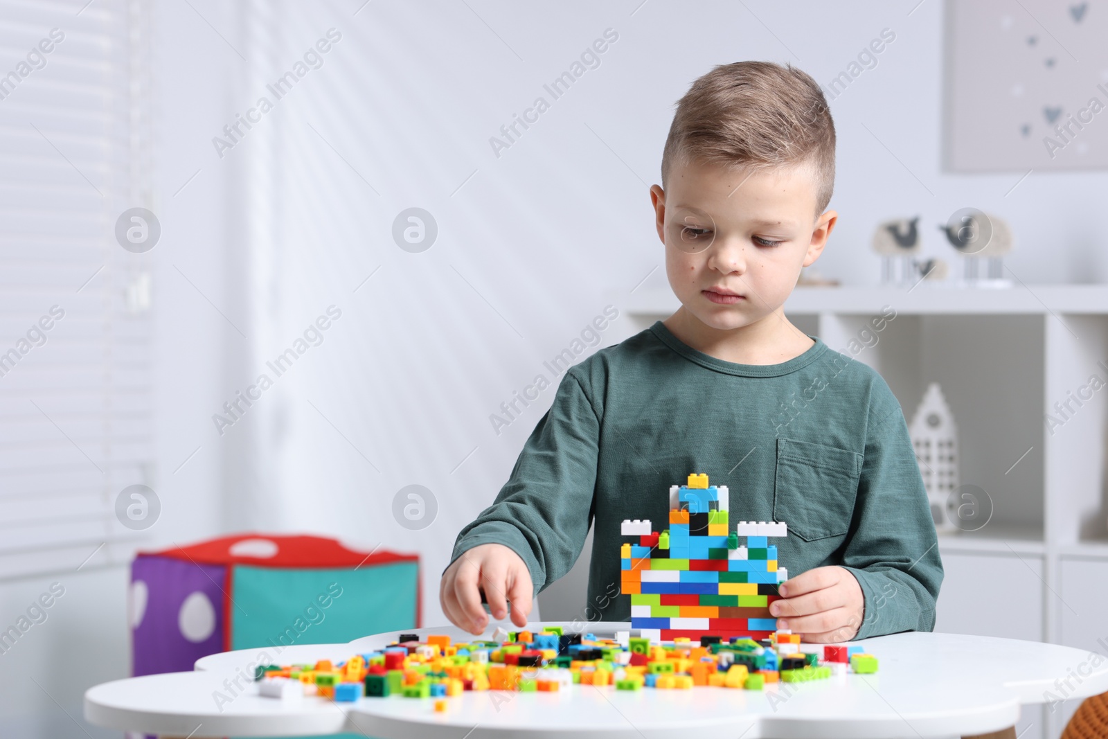 Photo of Cute boy playing with building blocks at white table indoors. Space for text